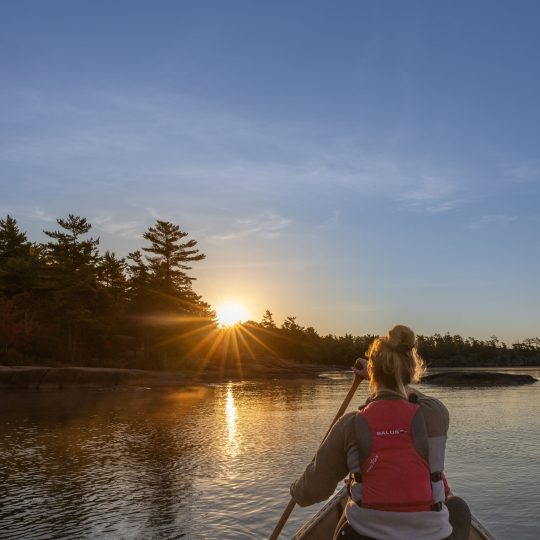 A lady paddling a canoe at sunset.